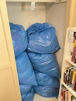 Six large blue trash bags stacked in closet