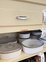 Shelf containing multiple white stoneware CorningWare French White dishes with glass lids