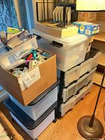Stack of plastic drawers, plastic totes, cardboard box filled with stationery and craft items