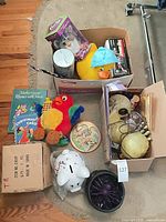 Overview of lot showing boxed Furby, rubber duck, plush parrot, RC car, books, piggy bank, spider toy and boxes
