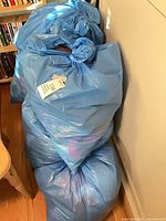 Three stacked blue plastic garbage bags filled with clothing
