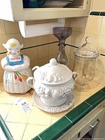 Group shot showing all four items: Dutch girl cookie jar, glass apothecary jar, smoky glass candlestick, white ceramic tureen on matching plate
