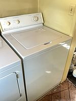 Front and top view of Maytag top-load washing machine beside dryer