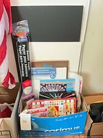 Box of assorted art supplies showing canvases, banner roll, paint bottles, pens