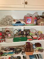 Wide view of three shelves showing mixture of ornaments, tins, ribbons, boxes