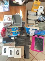 Overview of lot showing book cover, keyboard, smart bands, smartphone, writing tablet, chargers, boxed items