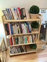 Full view of pine bookcase with books and faux plants on each shelf