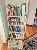 Front view of narrow bookshelf filled with books, magazines on floor