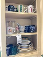 Overview of shelves showing assorted mugs, glass carafes, mortar & pestle, blue floral mugs, stacked plates and bowls