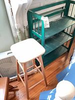 Wood bar stool, teal bookcase, partial view of white box fan