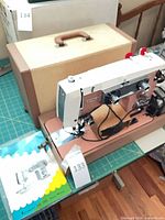 Sewing machine on base alongside tan case and manual