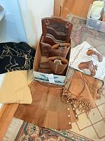 Group shot showing all items: boots in box, wooden rack, scarf, skirt, fringe bag, sweater, white cloth
