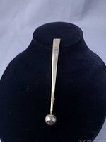 Front view of gold-tone exclamation mark brooch on display stand