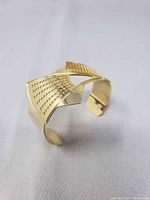 Gold tone cuff bracelet angled view showing perforated diamond panels and open back