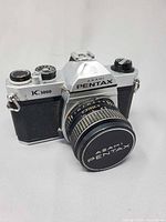 Front three-quarter view of Asahi Pentax K1000 body with mounted lens and cap