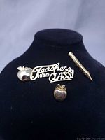 All three gold-tone teacher pins displayed on stand