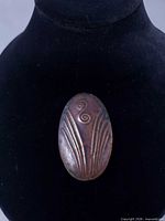 Front view of oval copper brooch on display form