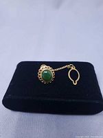 front view of tie tack showing green cabochon and chain