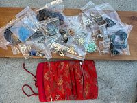 assorted costume jewelry pieces in plastic bags and red brocade travel jewelry roll pouch