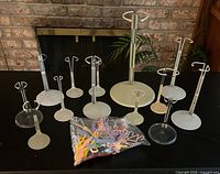 Collection of doll stands of various sizes and bag of colourful plastic hangers on tabletop