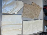All linen pieces laid out: ivory placemats with tags, ivory square and octagonal centerpieces, beige square pieces