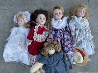 Five assorted vintage dolls laid on concrete surface