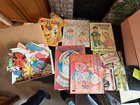 Group of nine paper doll books spread out with box of loose cut-outs