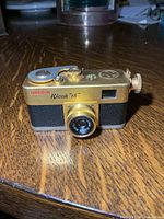 Front view of gold Ricoh 16 camera showing lens, viewfinder window and branding