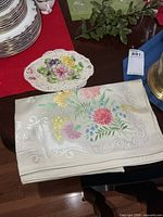Folded floral linen tablecloth beside porcelain centerpiece dish