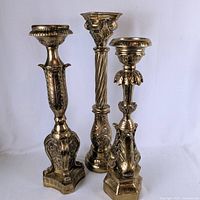 All three gold tone pillar candle holders standing together showing relative heights and ornate designs