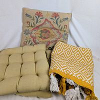 Group shot of pillow, two chair pads and folded rug showing textures and colours