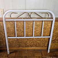 Full view of white tubular metal headboard with brass accents leaning against wall