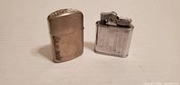 Both metal pocket lighters side by side displaying design, finish and wear