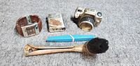 All five items grouped: wristwatch, lighter, camera, pen, brush