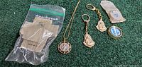 All jewelry items on green surface: necklace, two keychains, blue medal, clear bag with envelopes
