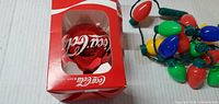 Coca-Cola ornament boxed beside colourful bulb garland