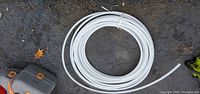 Coiled white plastic tubing on asphalt with tool cases nearby