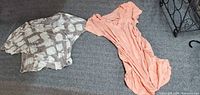 Both blouses laid flat on grey surface: peach ruched blouse on right, grey patterned blouse on left