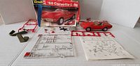 Open box contents laid out: partially built red Corvette, sprues, chrome tree, instruction sheet, box