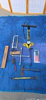 All items laid out on blue blanket, showing pump, levels, hacksaw, wrench, hatchet, square, packaged pliers