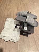 Slide sandals on top of box with tissue paper and hang tag visible