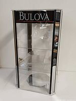 Front view of Bulova clear acrylic display cabinet showing door, shelves and logo