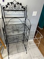 Full view of black baker’s rack beside white wire frame