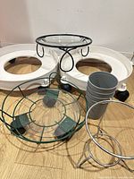 Overview of two white rolling caddies, black metal glass-top stand, green metal glass-top stand, chrome ring stand, and stack of grey pots