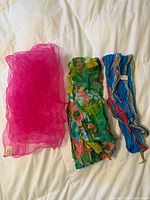 Three scarves laid out: pink sheer, green crinkled, blue pleated