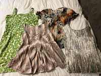 Four garments laid out: green dress, pink striped Floreat top, sheer multicolour blouse, grey stripe top