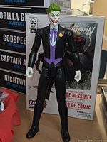 Front view of 12-inch Joker action figure standing, box art behind