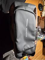 front of black sling shoulder bag showing white FASHION text