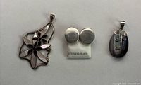 Front of three sterling silver jewelry pieces: floral pendant, round clip-on earrings, abalone pendant