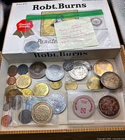 Open Robert Burns cigar box showing assorted coins and tokens in sleeves and loose